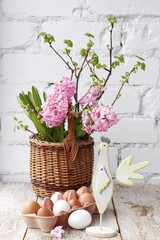 Easter still life. Pink hyacinths in a basket and chicken eggs on a background of a white brick wall.