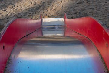 Slide with shiny smooth metal base and wooden red handrails descends steeply down to surface...