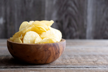 Homemade potato chips with salt lie in a wooden bowl and stand on a wooden table. Close-up. Place for text