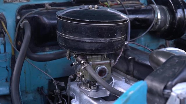 Old carburetor engine runs in retro blue car. View of the engine compartment of old car.