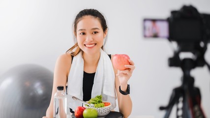 Beautiful asian woman healthy blogger is showing fruit and clean diet food. In front of the camera to recording vlog video live streaming at home.Fitness influencer on social media online.