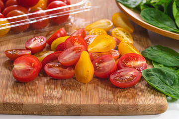 Sliced red and yellow tomatoes, and baby spinach close up on a wooden cutting board