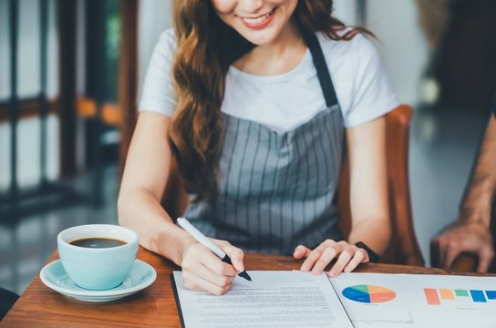 Asian women coffee shop owner is signing the contract. Start a new business On the table with a coffee cup and data sheets paper.Small business finance concepts.Vintage tone.