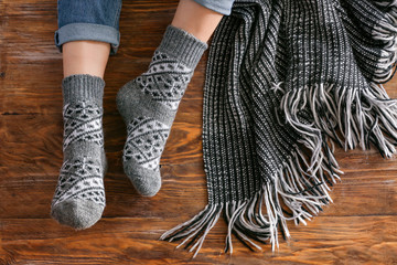 Legs of woman in knitted socks and plaid on wooden background