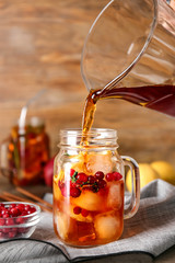 Pouring of tasty tea into mason jar on table