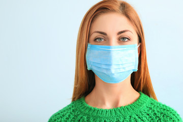 Young woman with protective mask on light background. Concept of epidemic