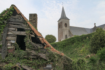  the village church behind a hedge with an old decayed barn in the foreground