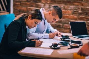 Young couple signing paper contract together at business meeting in a cafe bar