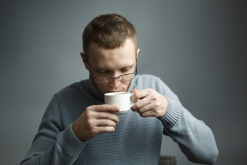 Man in sweater and glasses drinking coffee.