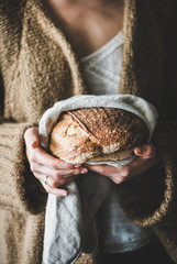 Young woman holding freshly baked healthy wheat Swedish bread round loaf in tpwel in hands, selective focus