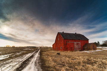 Stunning dramatic sunsets in rural farm country with barns and cold fields with rainbow.