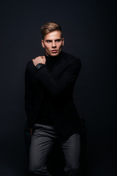 Formally dressed man with sharp jawline in his 20's posing in a studio in front of a black background.