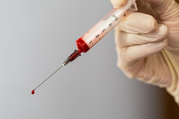 Syringe with a blood sample. A drop of blood at the end of the needle. Blood chemistry. Blood test for viruses.