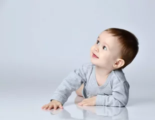 Fototapeten Little baby boy toddler in grey casual jumpsuit and barefoot lying on floor, smiling and looking up © FAB.1