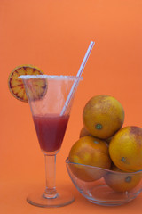 Decorated glass of a cocktail with blood oranges juice next to a bowl with blood oranges