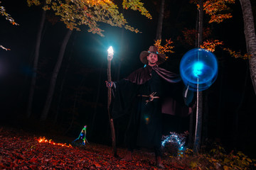 Sorcerer (magician) casting a spell while standing in the magical woods. Holding his magical staff....