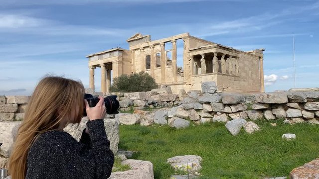 A pretty blonde traveler girl takes photos of the Parthenon Temple at the Acropolis of Athens