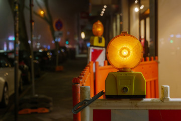 Night and close up view at orange caution light and plastic barriers to warn for construction site...