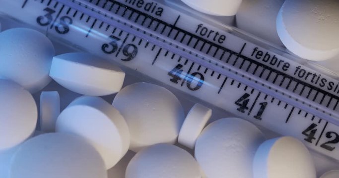 Slow motion pan over a clinical thermometer and white pills. Italian writing on fever thermometer from normal to strongest fever