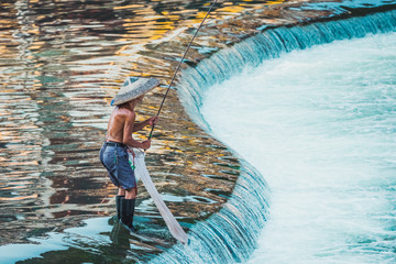 Fisherman with a traditional triangular chinese hat standing in waters of Tuo river flowing through the centre of ancient city Fenghuang Old Town