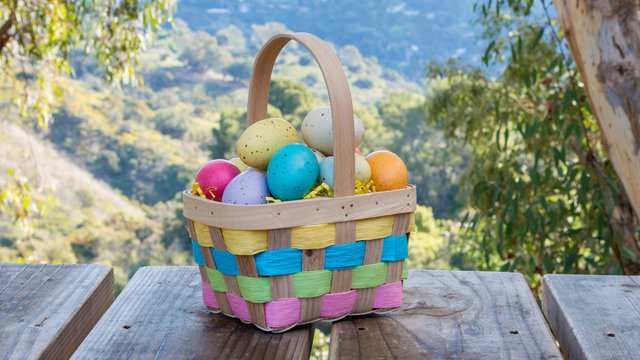 a wicker Easter basket filled with speckled Easter eggs sitting on a wooden picnic table overlooking lush scenic hills with copy space