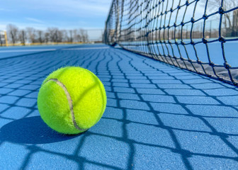 Tennis ball on a soft blue court next to the net. outside tennis court