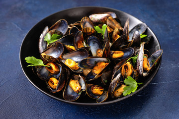 Close up of a plate with steamed mussels on blue background