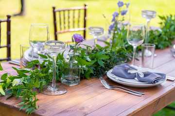 Beautifully decorated wooden table in a summer open-air cafe. Green branch and fresh flowers table decoration