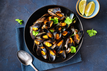 Cooked mussels in a plate with parsley and lemon on blue background