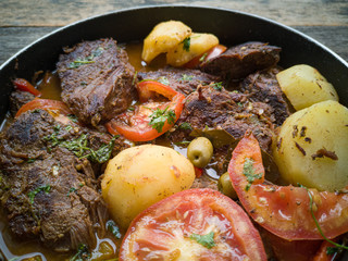 Meat with broth and vegetables in frying pan.