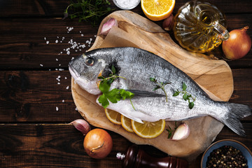 Top view of one raw fish on wooden board with ingredients