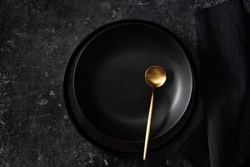 Top view of empty black plate with gold spoon on black background