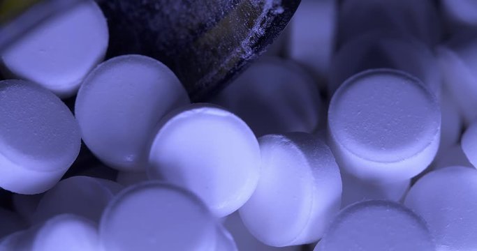 Panning over pills and glass medical bottle for medicinal drugs. Blue light illuminating painkiller pills and opioids causing the opioid crisis