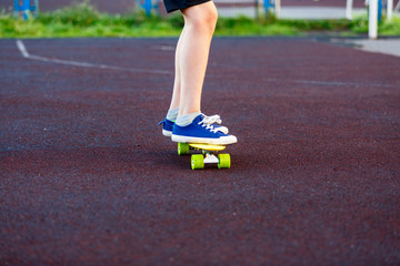 Close up legs in blue sneakers riding on yellow skateboard in motion. Active urban lifestyle of youth, training, hobby, activity concept. Active outdoor sport for kids. Child skateboarding.