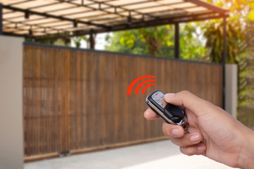 Closeup hand holding and using remote control to open or close the automatic wooden gate with home...