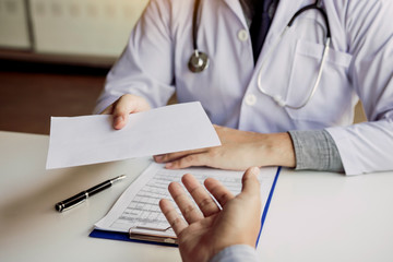 Asian male doctor talking in clinic room and handing a prescription to the patient.