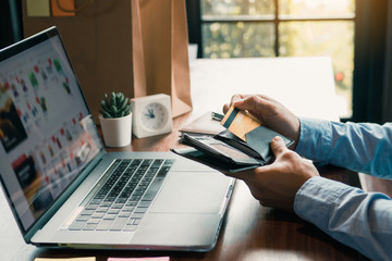 Asian man hand is pulling a credit card out of his pocket in order to complete online shopping on the computer.