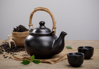 Cup of hot tea with teapot, green tea leaves and dried herbs on the wooden table with empty space,...