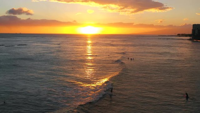 A surfer travels across the screen on a wave. The sunset radiates in the background. An Oahu activity is always better at sunset.