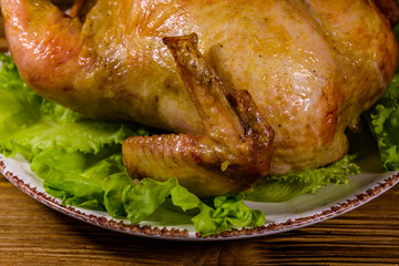 Plate with roasted whole chicken and lettuce leaves on a wooden table