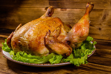 Plate with roasted whole chicken and lettuce leaves on a wooden table