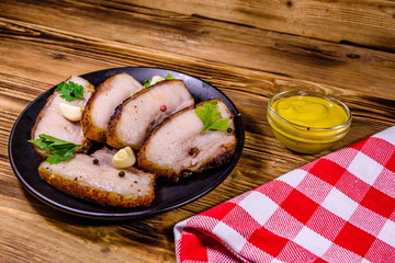Slices of baked pork belly, garlic and parsley on a black plate