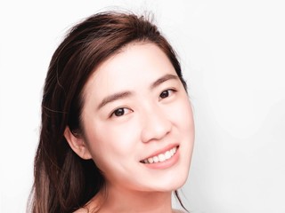 Naklejka premium young beautiful asian woman with clean and bright skin, Cosmetic Beauty Concept,hands touch on the cheek, smiling and friendly face isolated on grey background