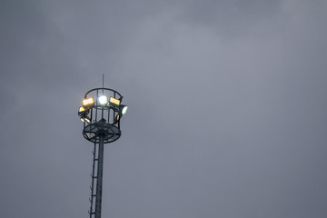 Lighting metal mast. LED spotlights. White and yellow light. Snow falls. Concept of night lighting.