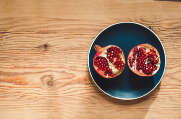 Top view - Two parts cut fresh red pomegranate with berries lying on a blue plate on a wooden table. Healthy eating. Copy space