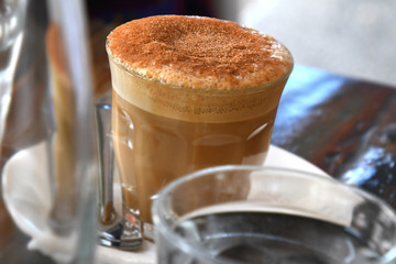 Frothy top coffee in glass at cafe table.