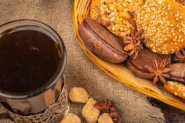 A glass of tea in a vintage Cup holder and cookies, chocolate cakes and star anise in a wicker basket on a background of rough homespun fabric. Close up.