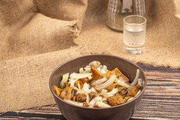 Pickled mushrooms with onion, shot of vodka and a carafe on the background of rough homespun...