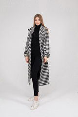 Full length stock photo of an elegant lady in black hat, stylish coat in crow s foot print, black tights and patent leather high heels. Model walking in fashionable look on white background. Isolate