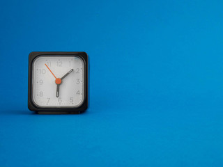 black table clock on the left, on a blue background